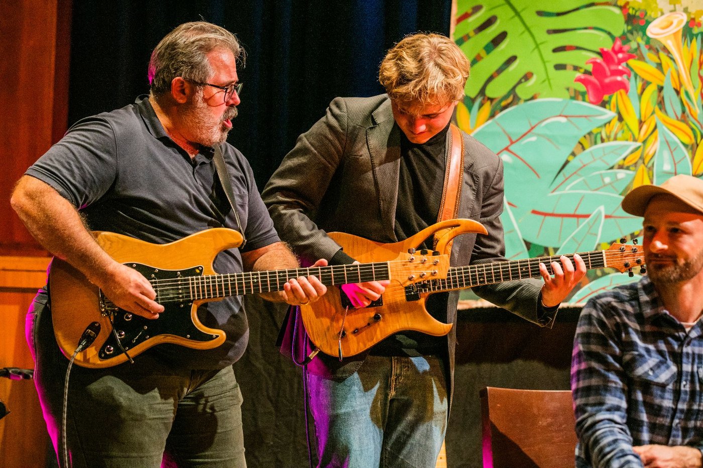 two guitarists playing together and a guy that looks in the distance